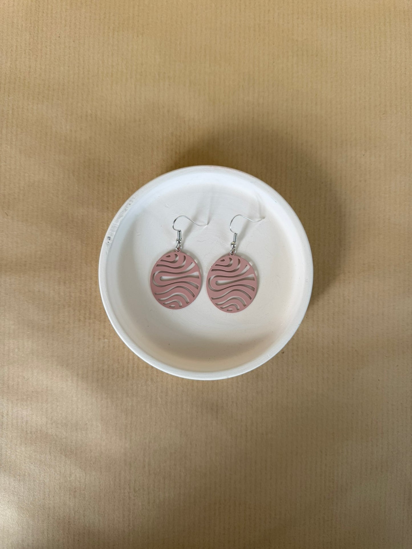 Pink Pair of earrings with wavy design in a white dish on a beige background
