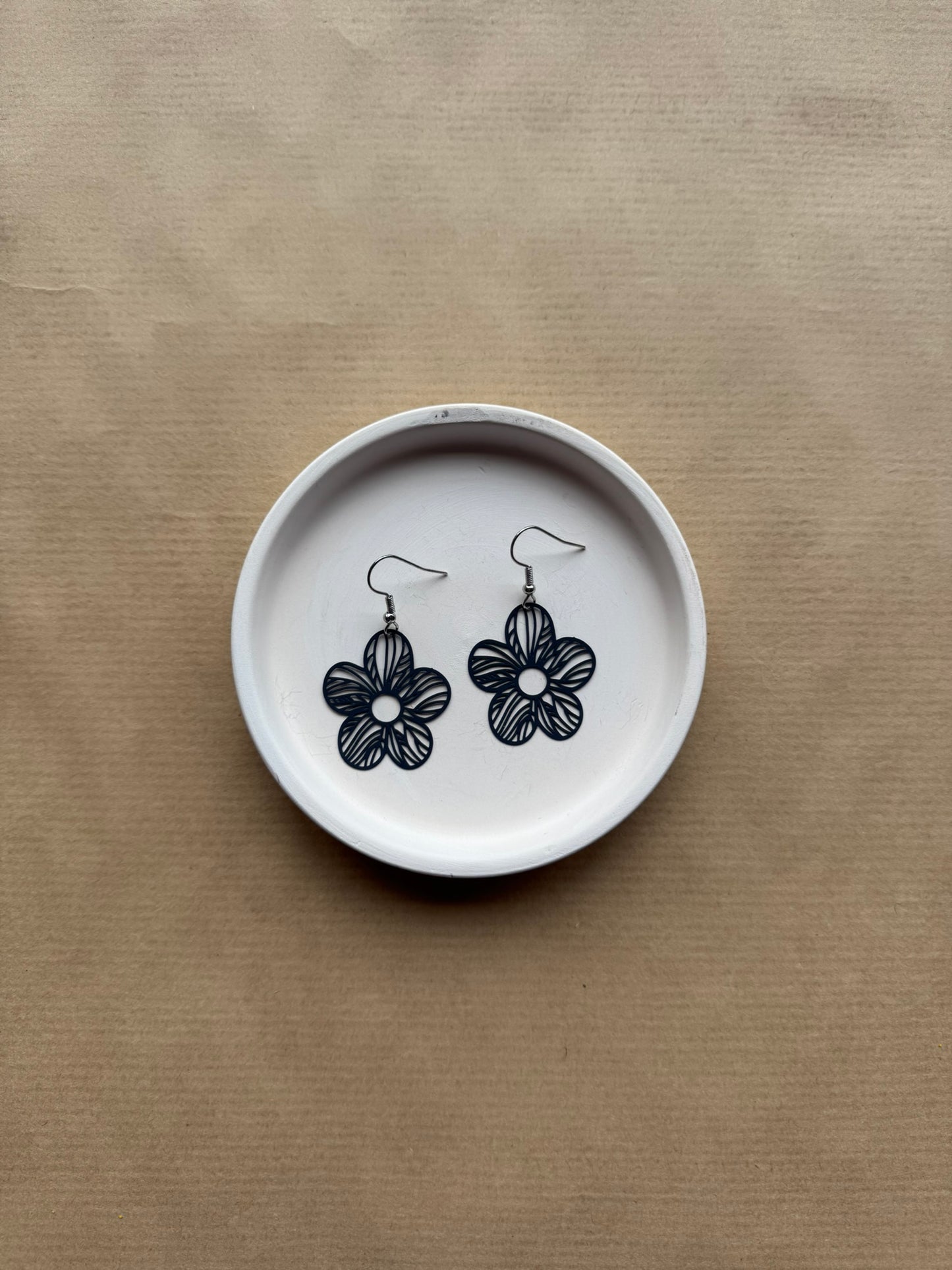 Flower-shaped earrings on a white dish with navy floral designs against a beige background