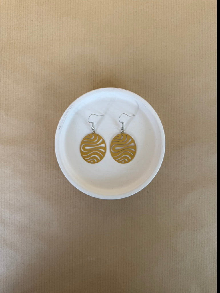 Yellow earrings on a white dish against a beige background