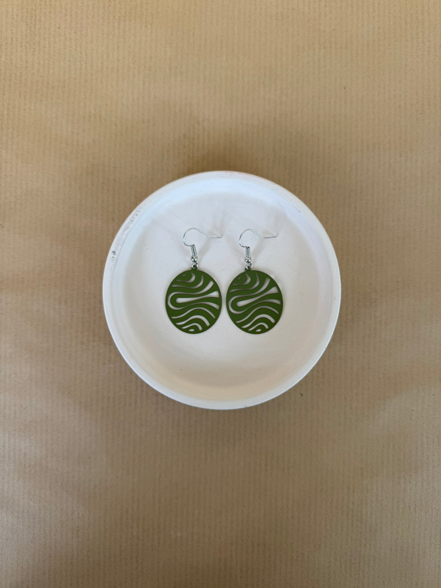 Green circular earrings on a white dish against a beige background
