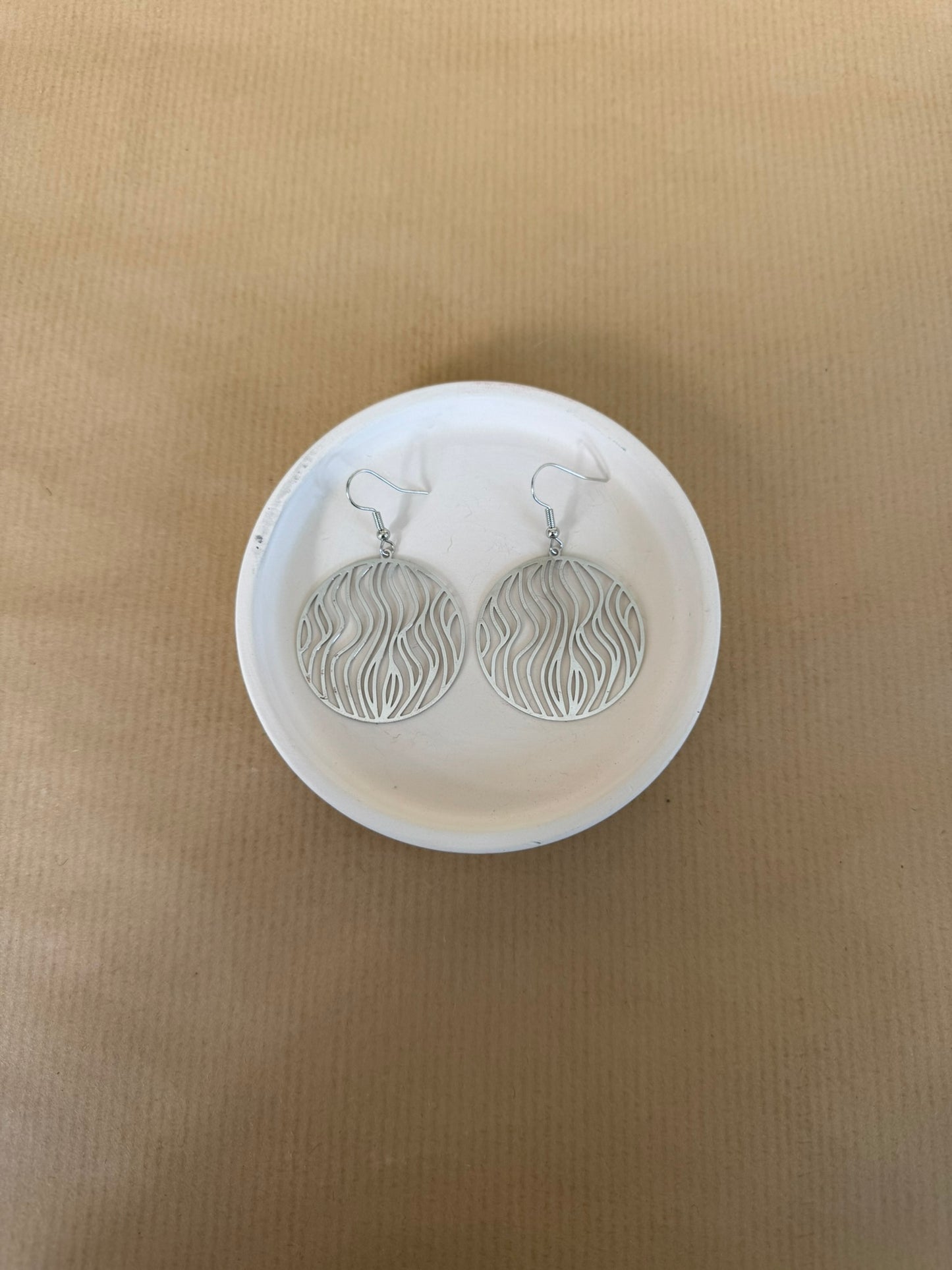 Silver earrings on a white circular stand against a beige background