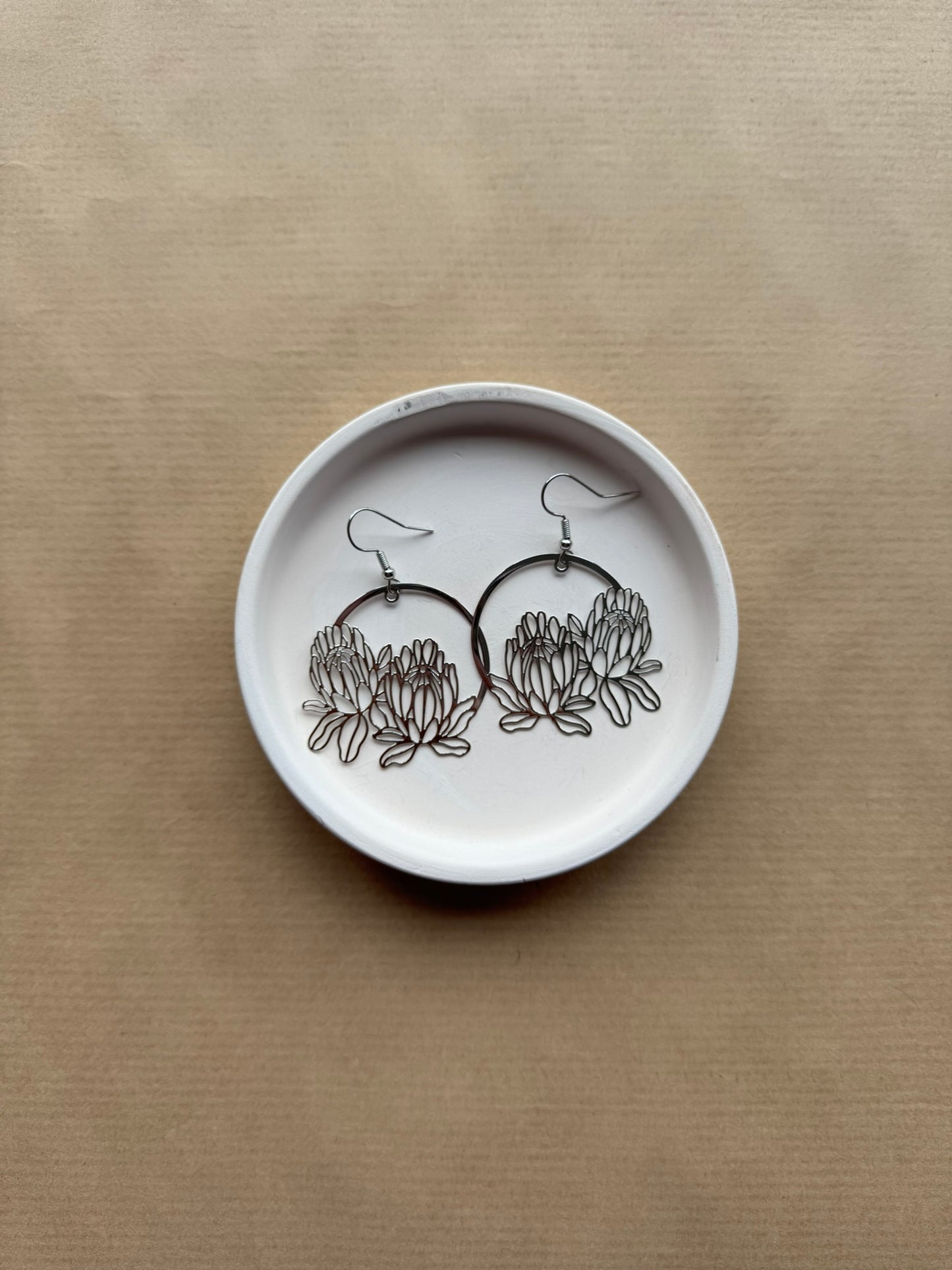 White dish with floral earrings on a beige background