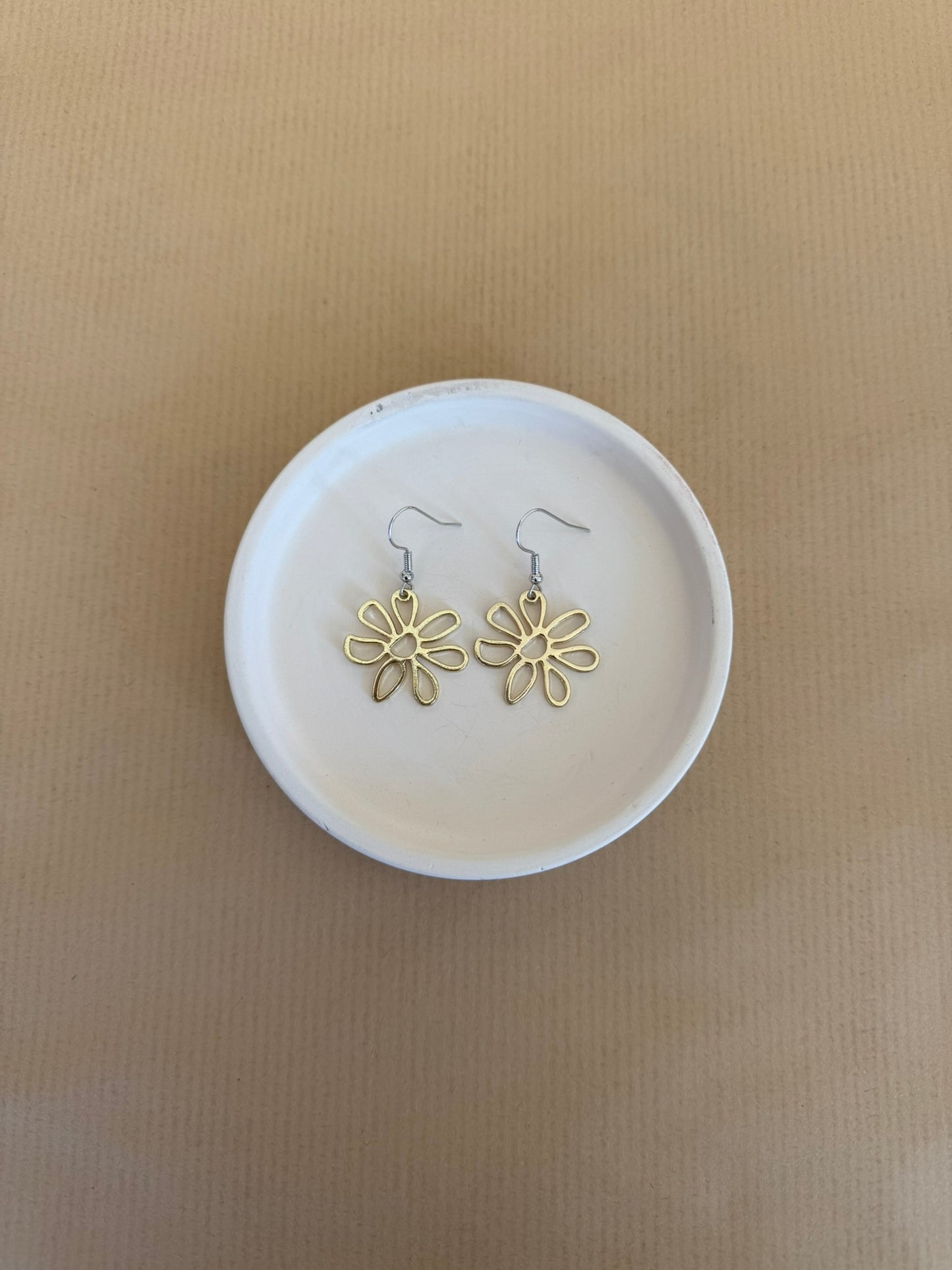 Gold flower-shaped earrings on a white dish with a beige background