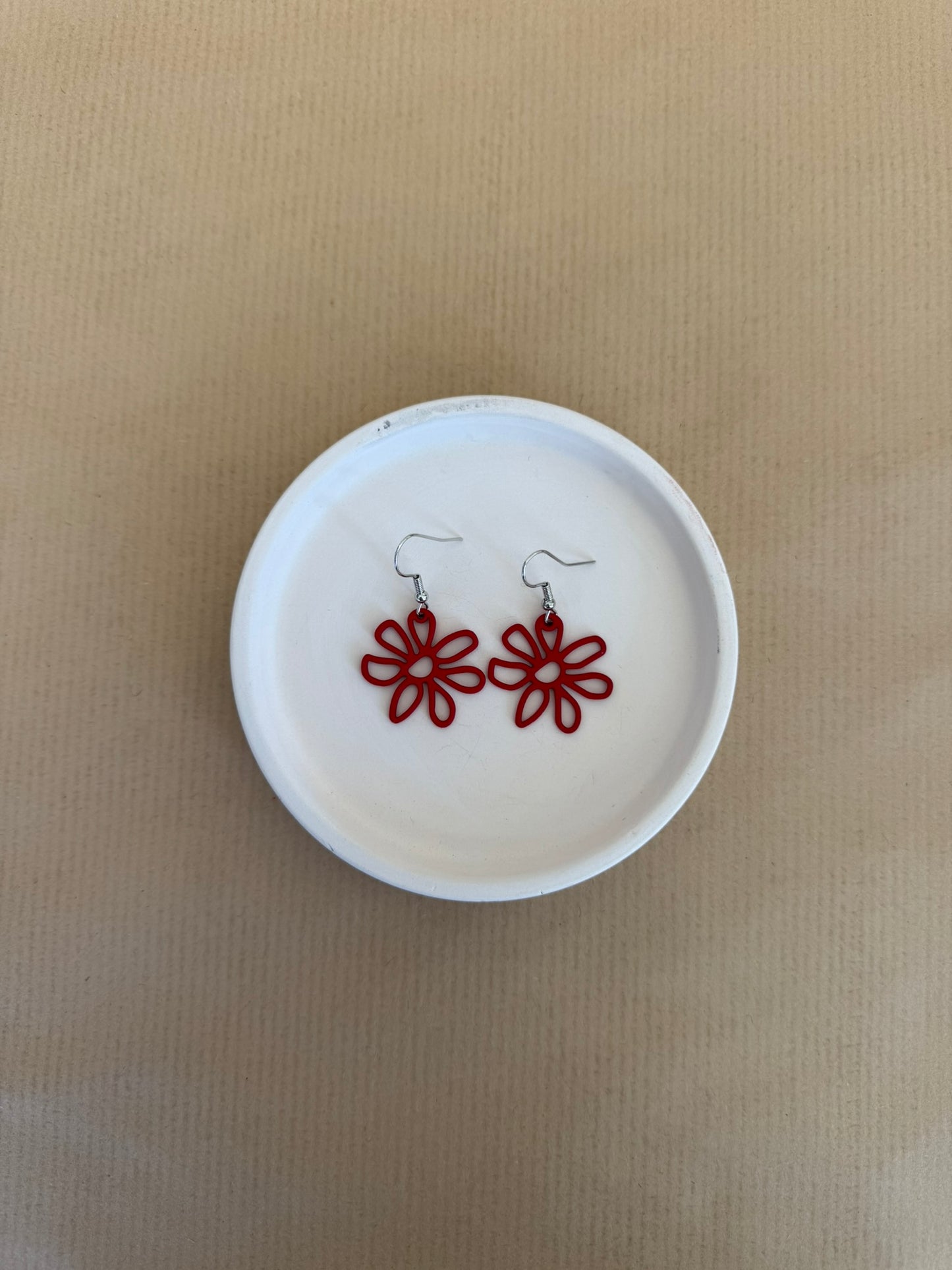 Red flower-shaped earrings on a white circular dish against a beige background