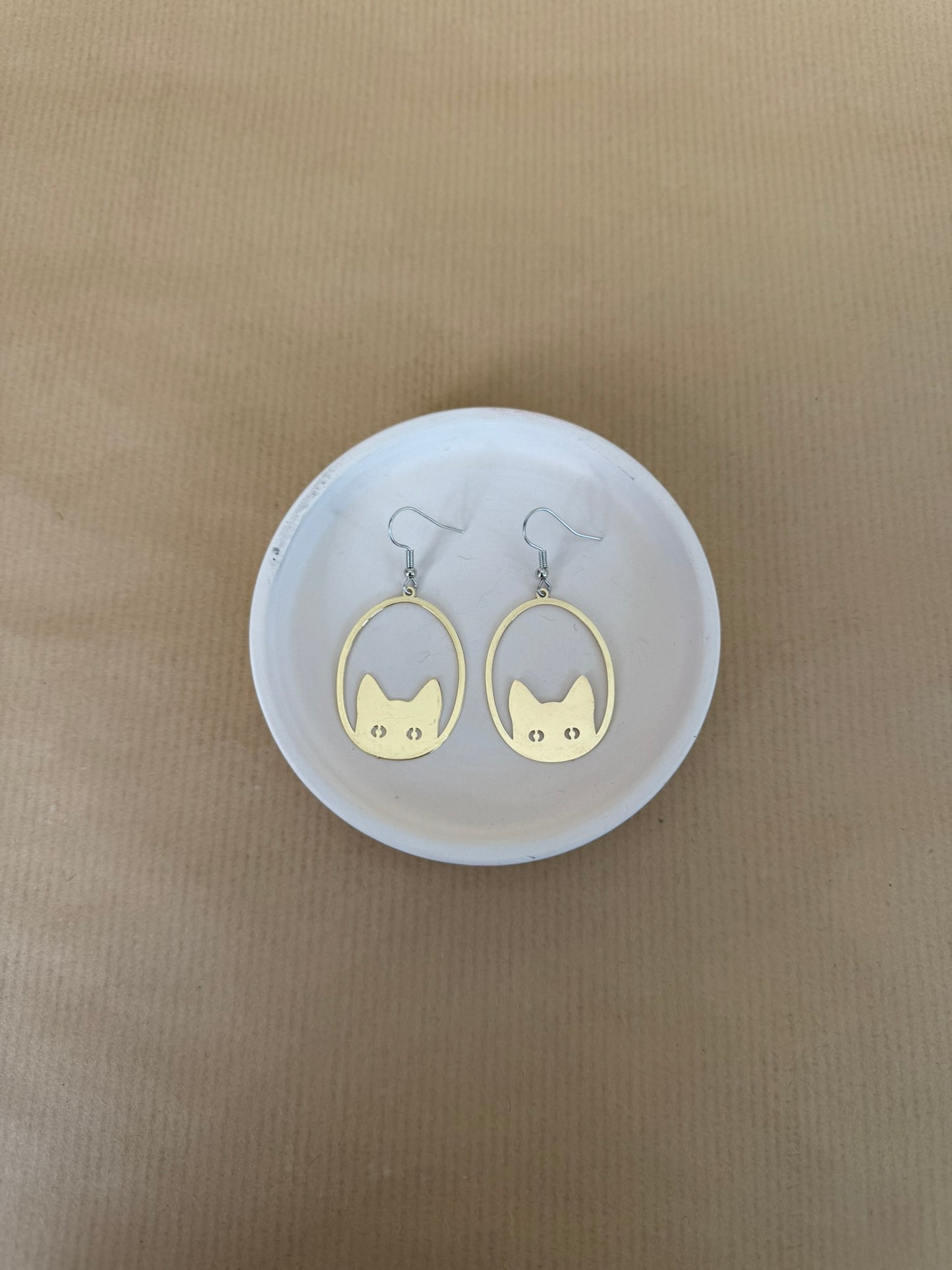 Gold cat-shaped earrings on a white circular stand against a beige background