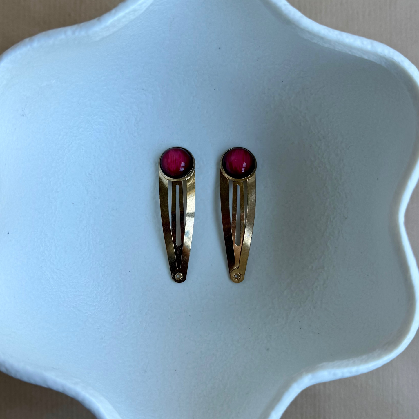 Two gold hair clips with red stones on a white ceramic dish.