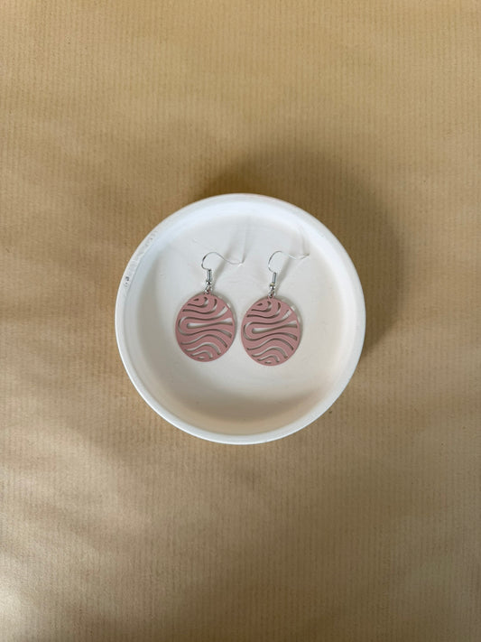 Pink Pair of earrings with wavy design in a white dish on a beige background