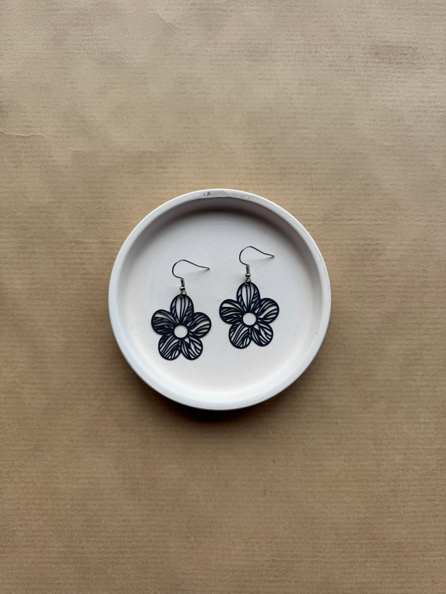 Flower-shaped earrings on a white dish with navy floral designs against a beige background