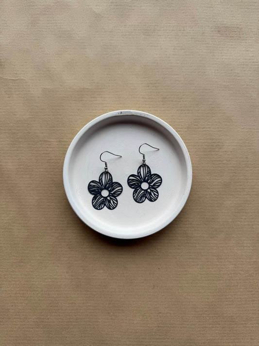 Flower-shaped earrings on a white dish with navy floral designs against a beige background