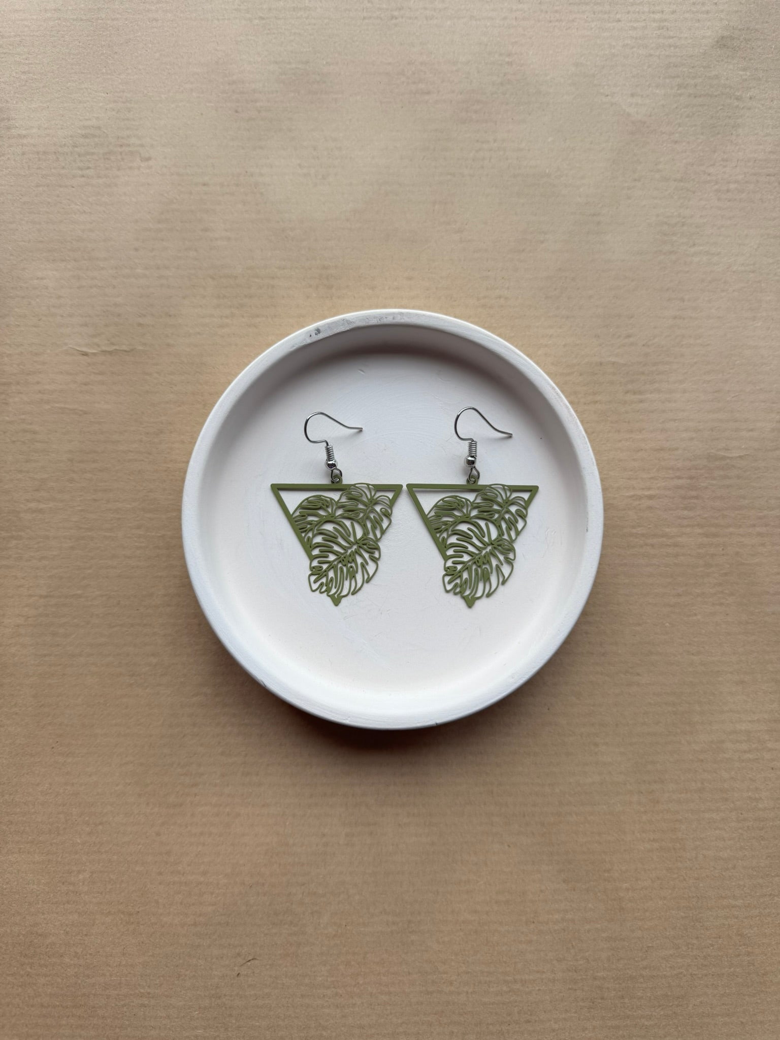 Pair of green leaf-shaped earrings on a white circular tray with a beige background