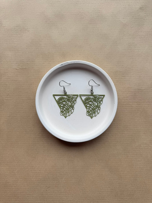 Pair of green leaf-shaped earrings on a white circular tray with a beige background