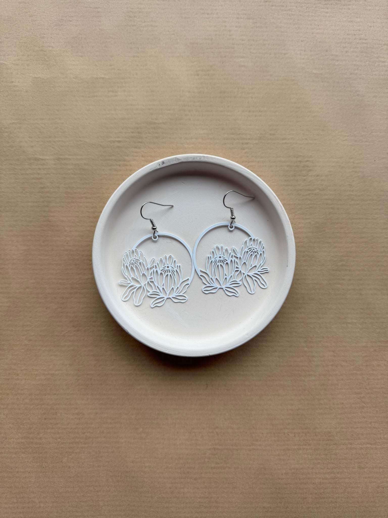 Pair of floral earrings on a round white stone surface with a beige background