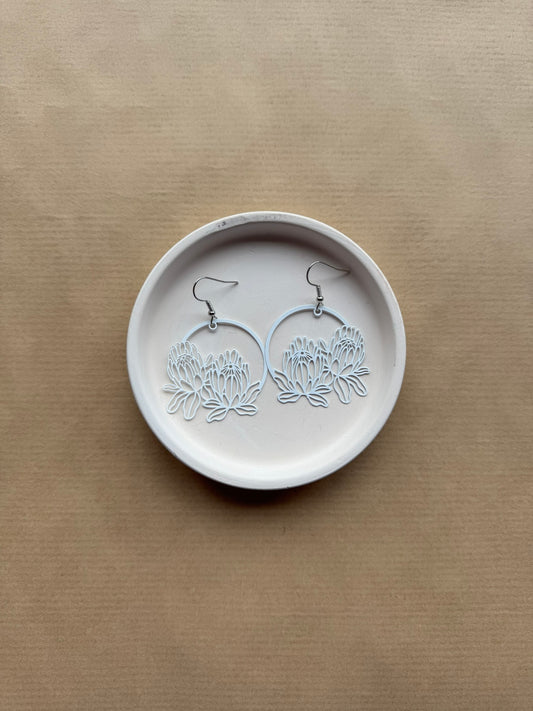 Pair of floral earrings on a round white stone surface with a beige background