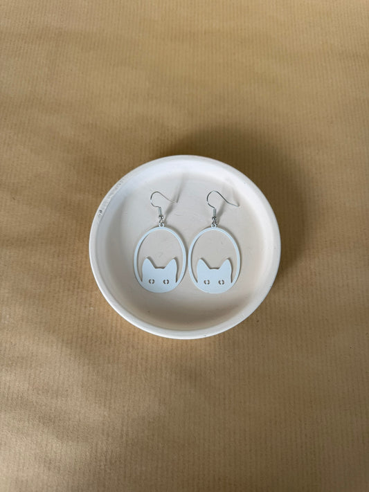 white Cat-shaped earrings on a white dish against a beige background