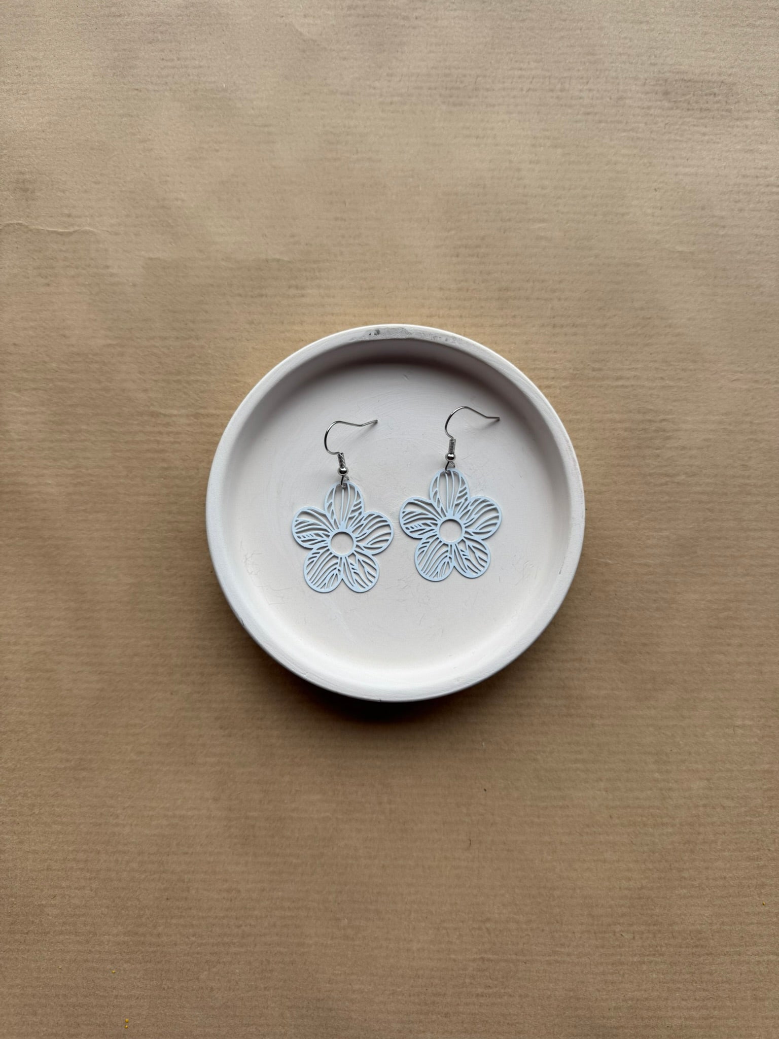 Floral earrings on a white dish against a beige background