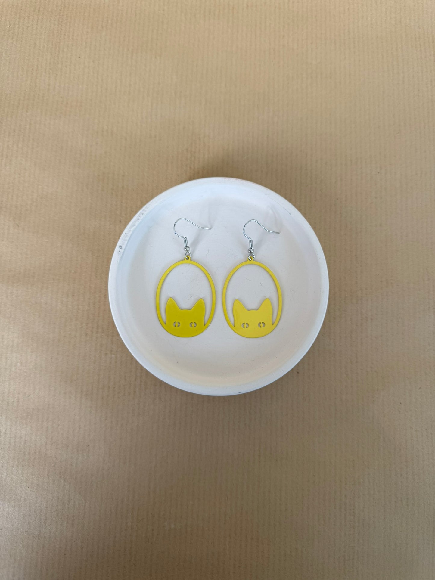 Yellow earrings on a white circular stand against a beige background
