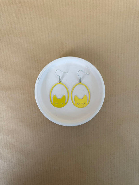 Yellow earrings on a white circular stand against a beige background