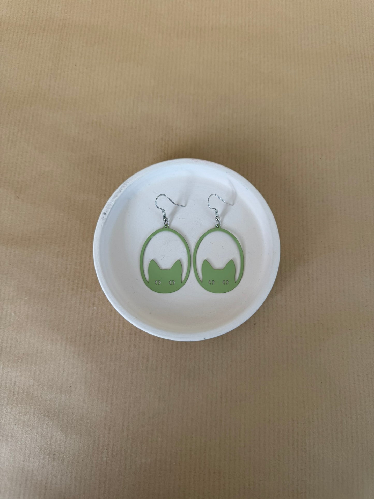 Green earrings on a matching round white dish against a beige background