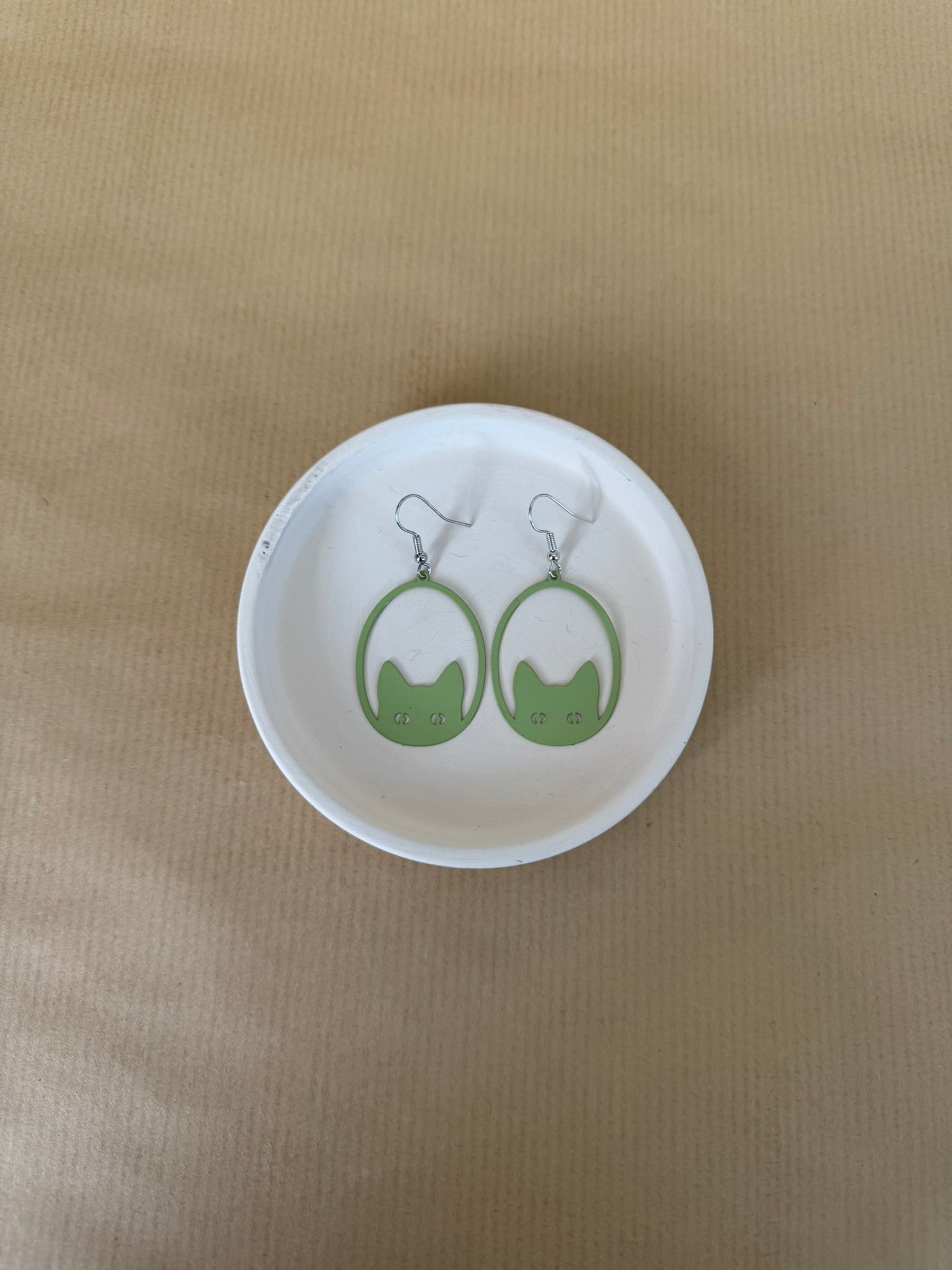 Green earrings on a matching round white dish against a beige background