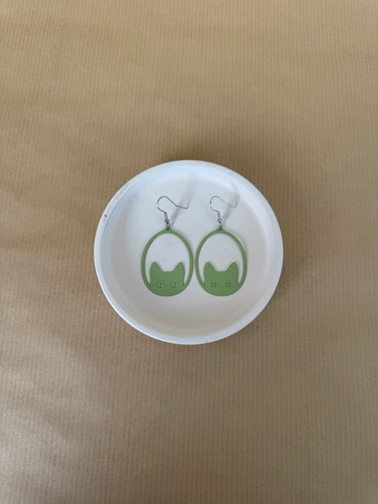 Green earrings on a matching round white dish against a beige background