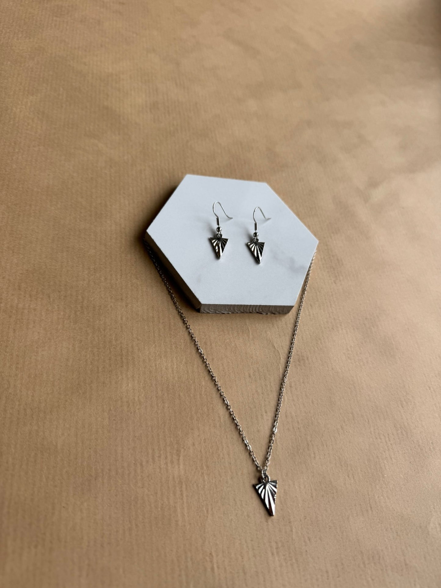 Necklace and earrings with arrow design on a hexagonal white stand against a beige background