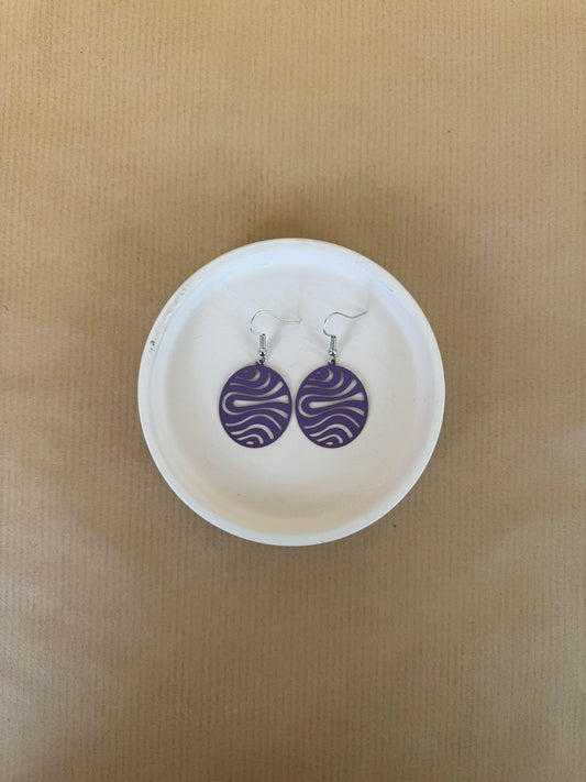 Pair of purple earrings on a white dish against a beige background