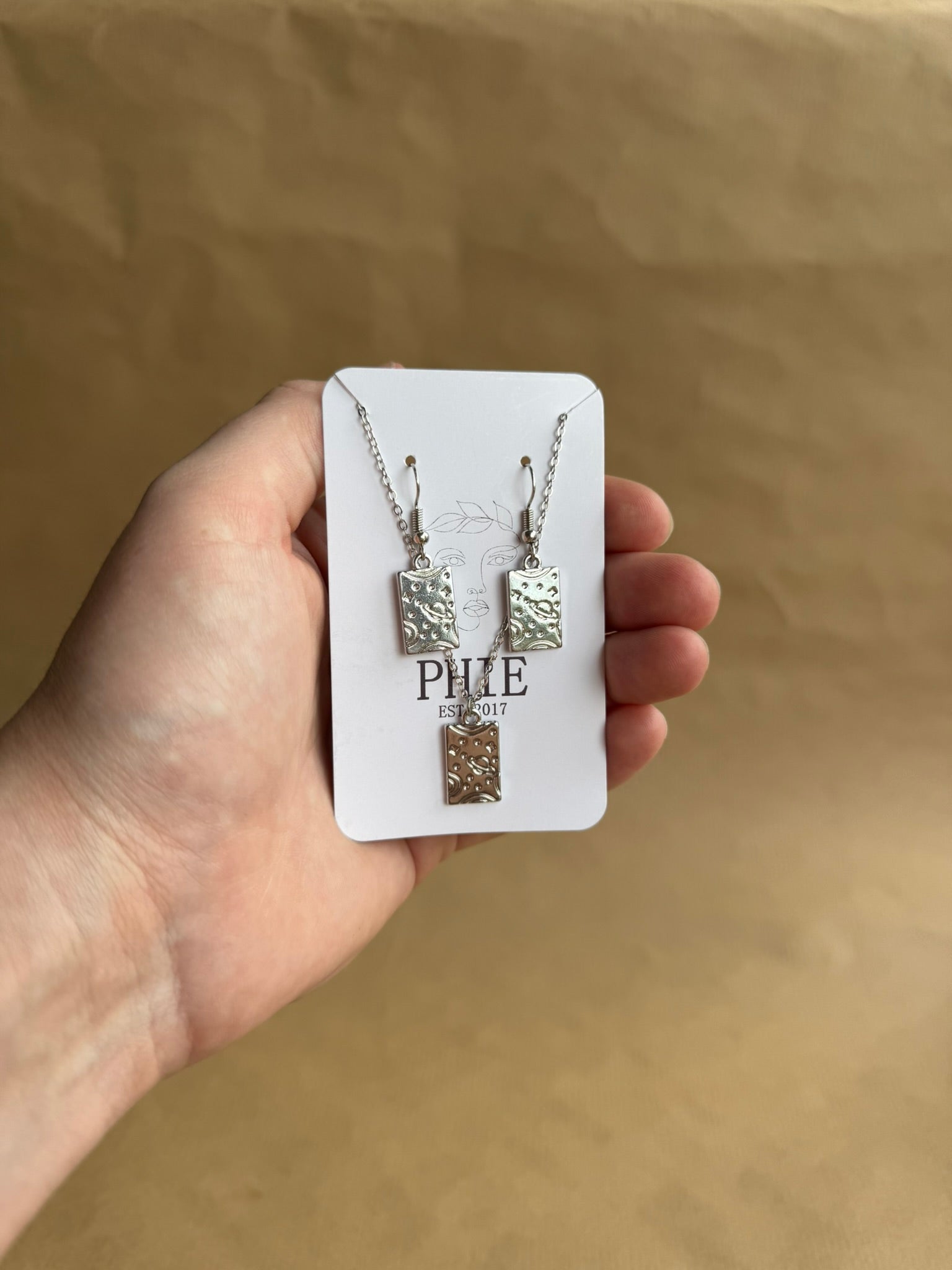 Hand holding a jewelry set on a beige background