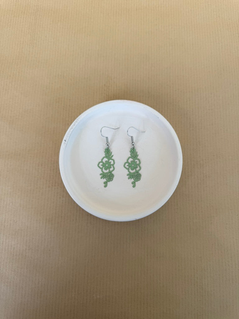 Light Green earrings on a white circular stand against a beige background