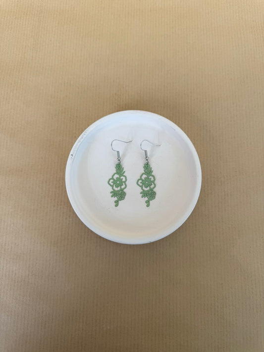 Light Green earrings on a white circular stand against a beige background