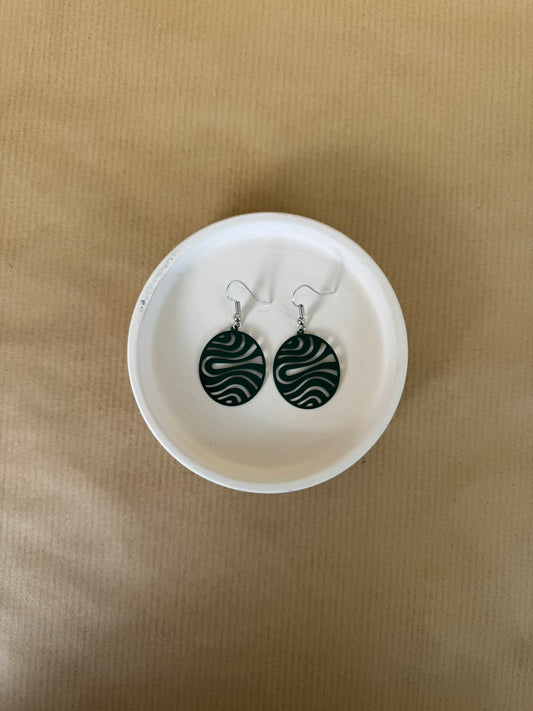 Green Pair of earrings on a white dish against a beige background