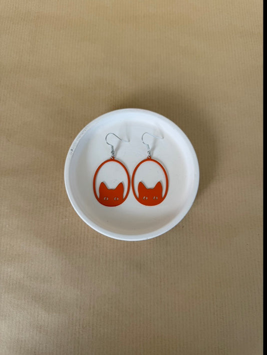 Pair of earrings with a cat design on a white dish against a beige background