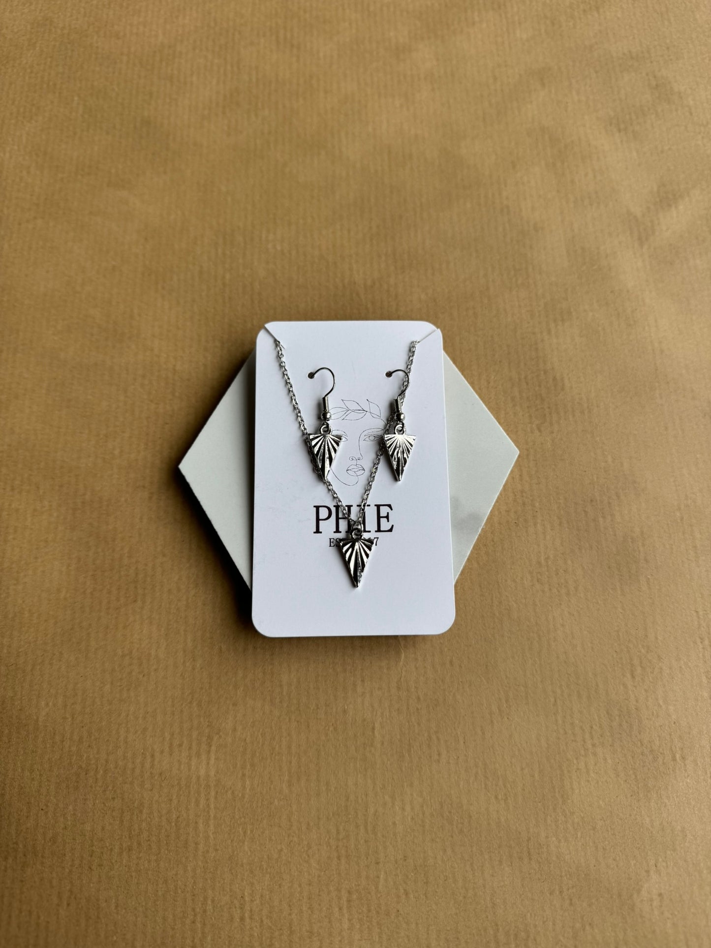 Necklace with leaf design on a white card with 'PHIE' branding, against a beige background