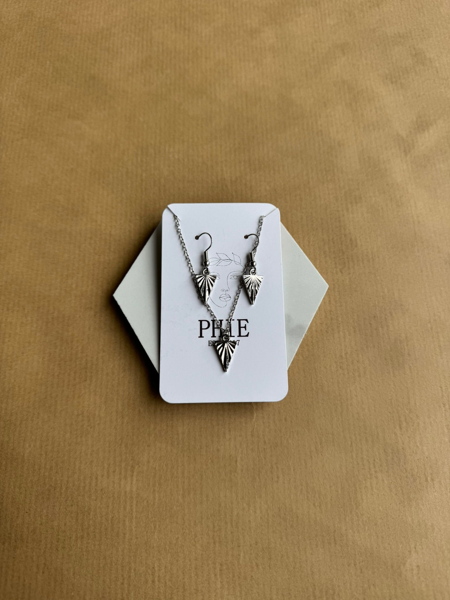Necklace with leaf design on a white card with 'PHIE' branding, against a beige background