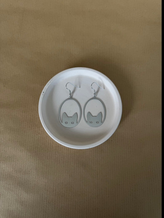 White dish with cat-shaped earrings on a beige background