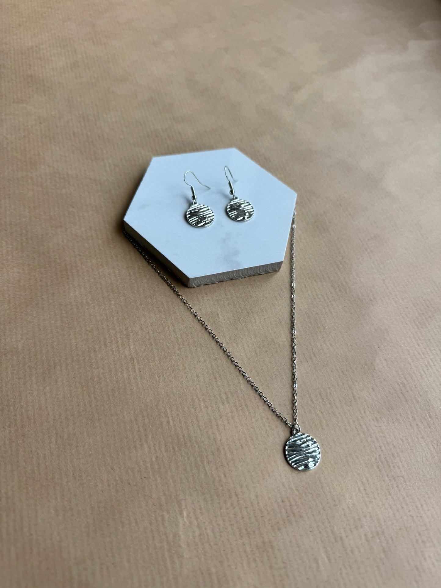 Silver necklace and earrings on a hexagonal gray stand against a beige background