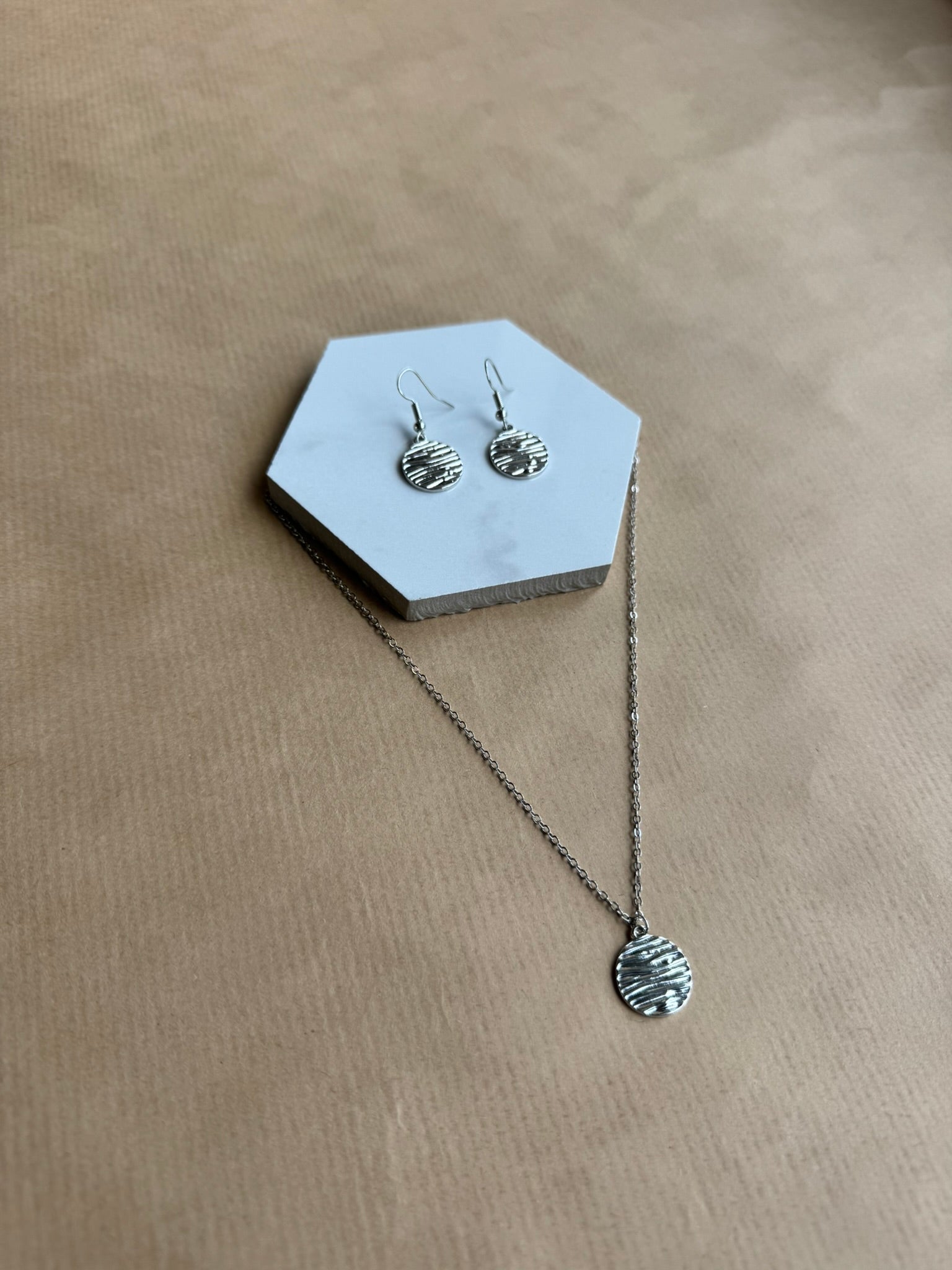 Silver necklace and earrings on a hexagonal gray stand against a beige background