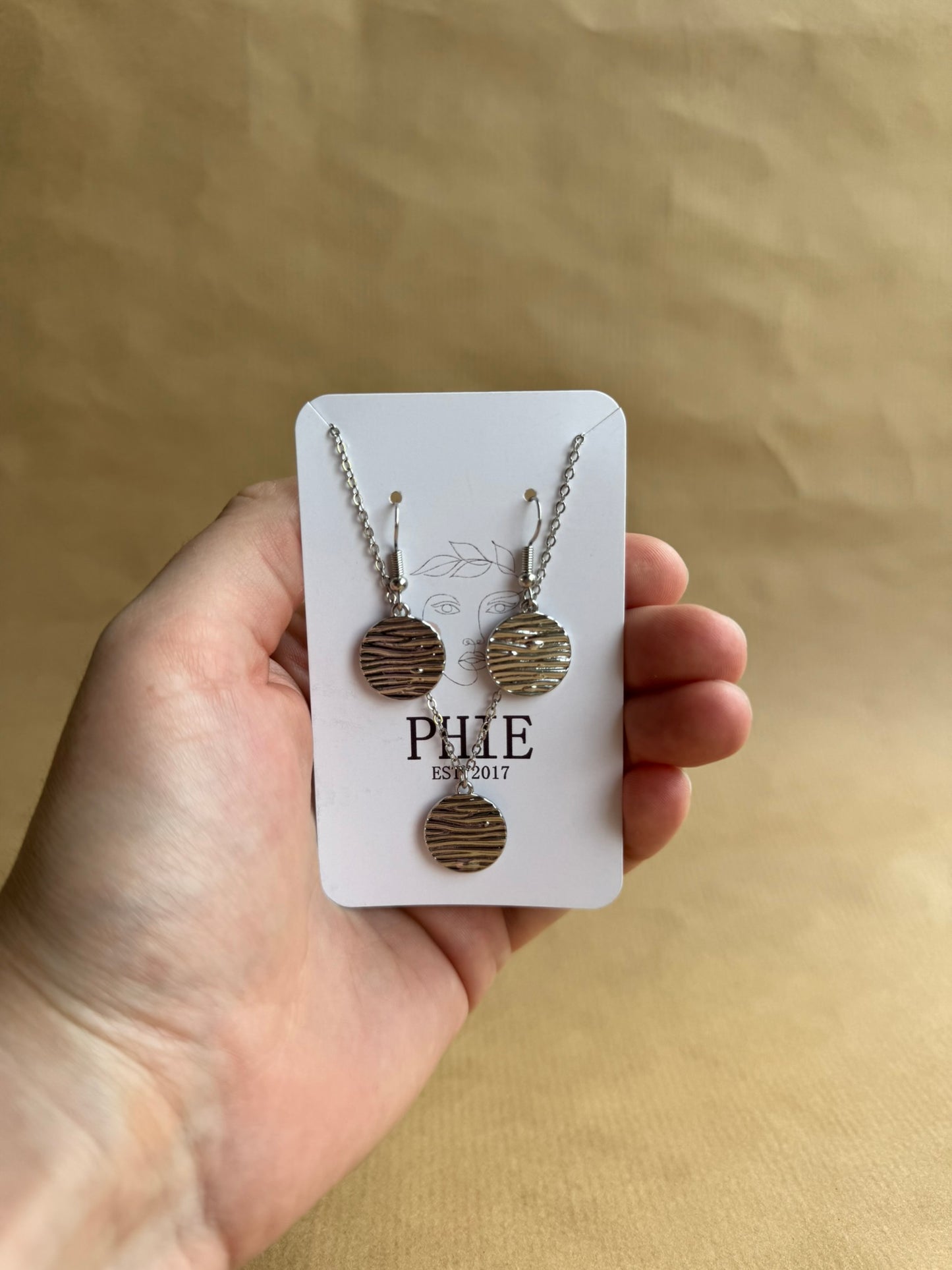 Hand holding a card with earrings and a necklace on a beige background