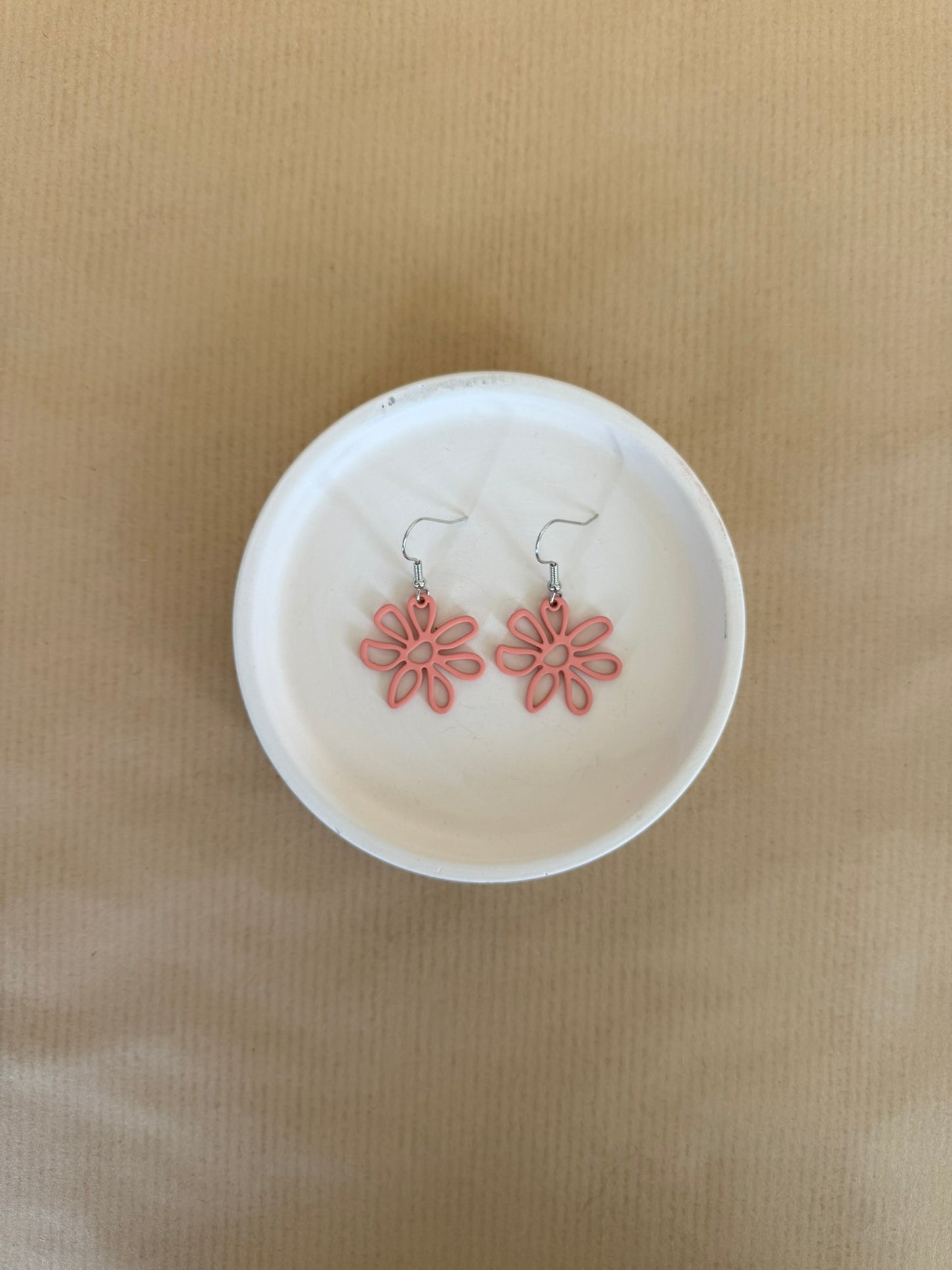 Pink flower-shaped earrings on a white dish against a beige background