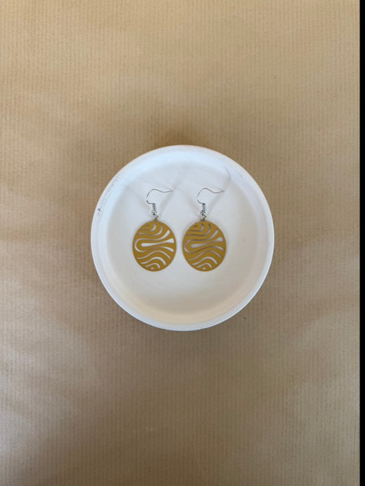 Yellow earrings on a white dish against a beige background