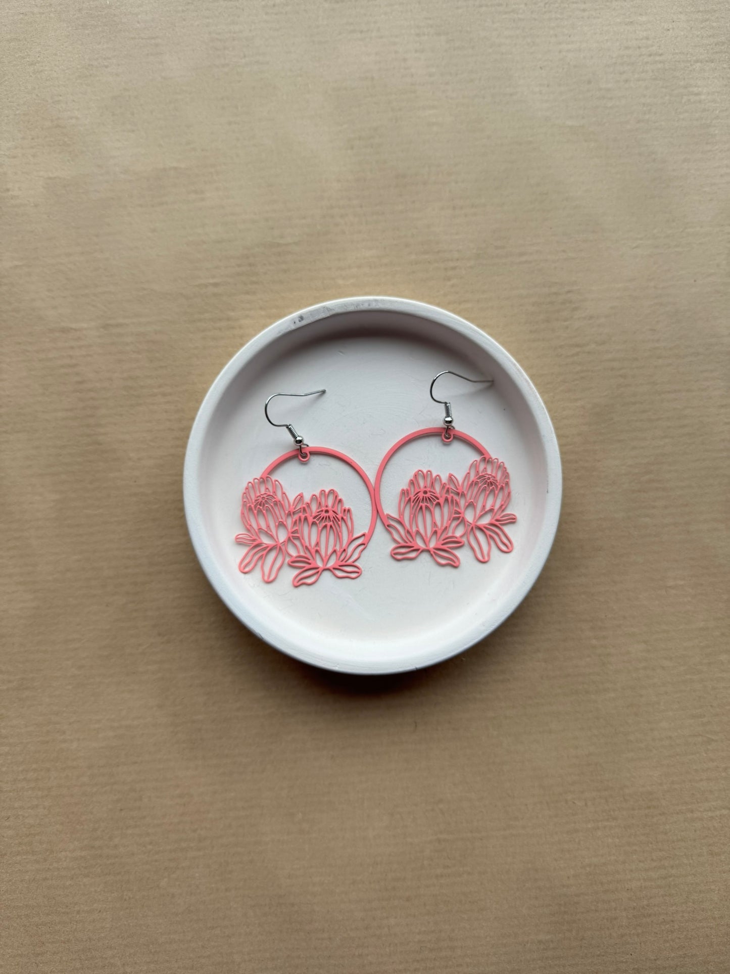 Pink floral hoop earrings on a white dish against a beige background