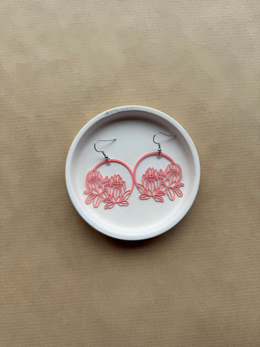 Pink floral hoop earrings on a white dish against a beige background