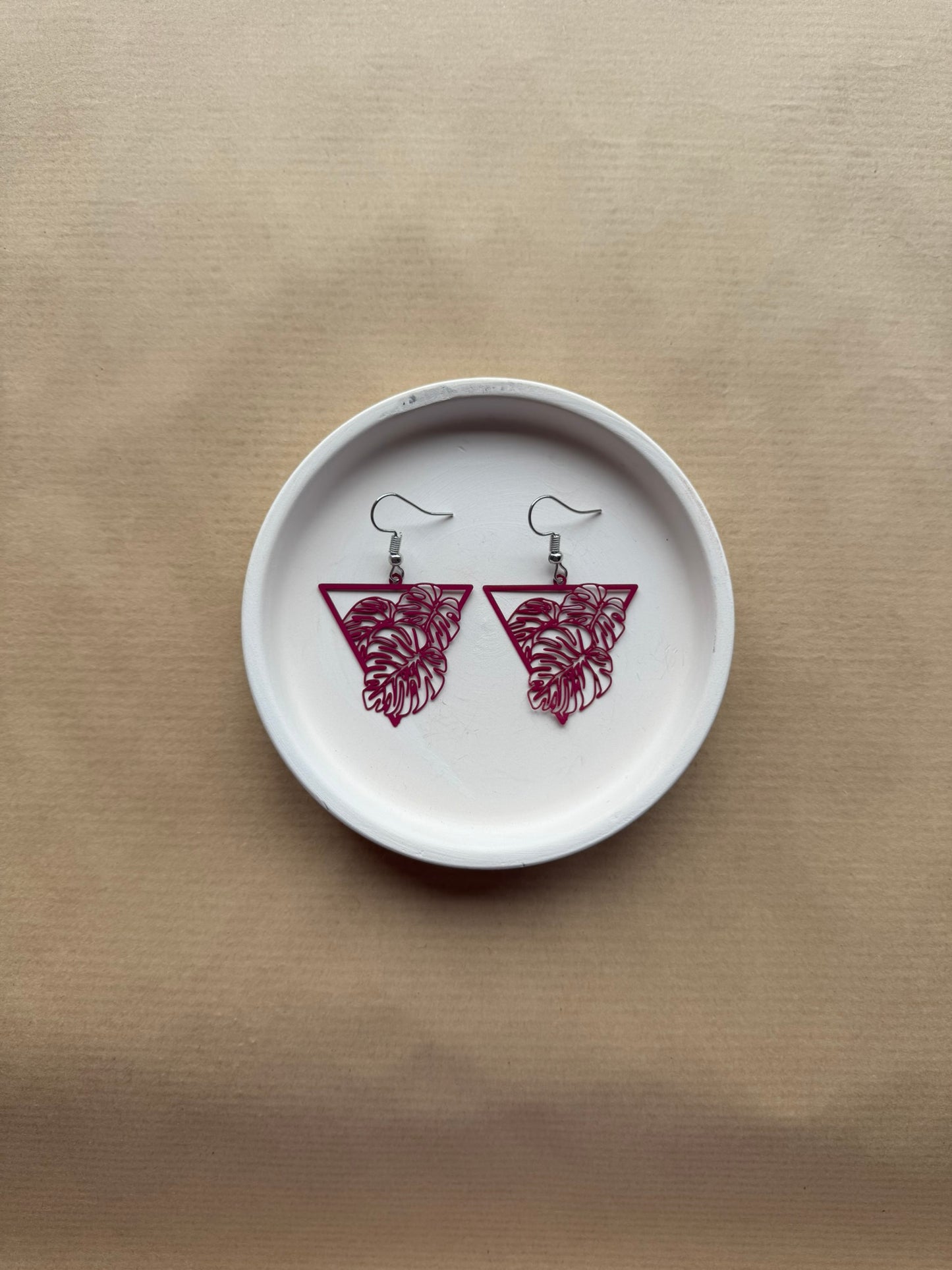 Pair of pink earrings on a white dish with a beige background