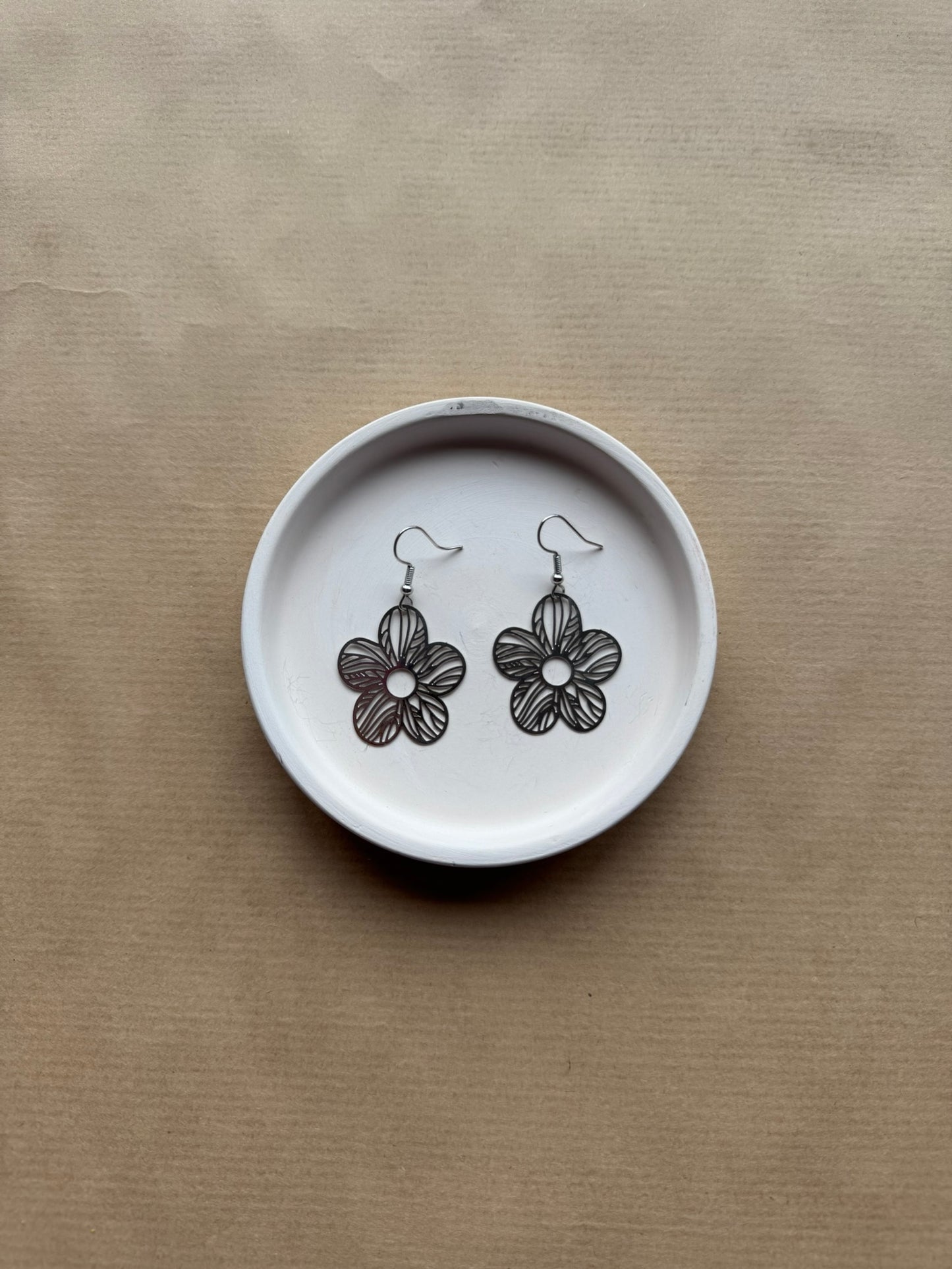 Flower-shaped earrings on a white dish with a beige background