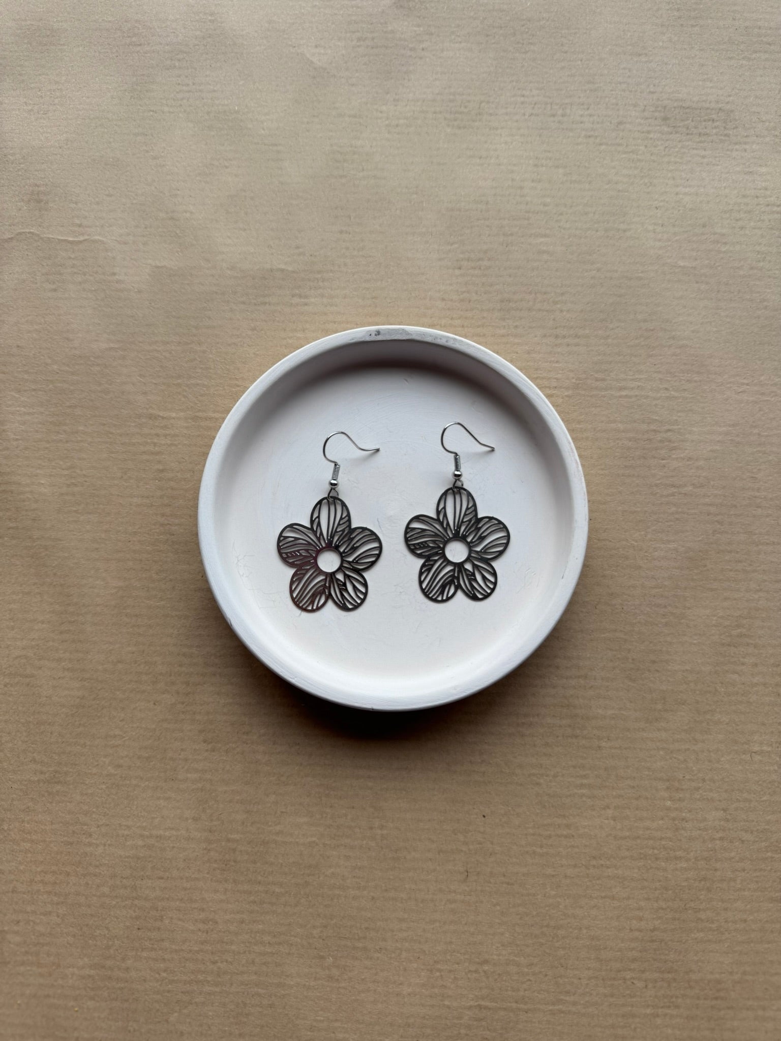 Flower-shaped earrings on a white dish with a beige background
