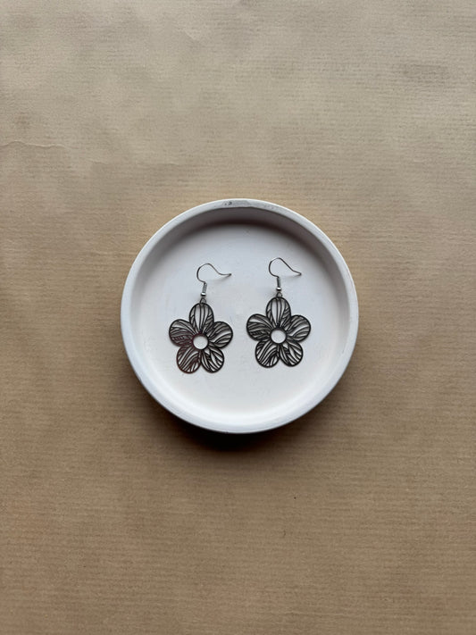 Flower-shaped earrings on a white dish with a beige background