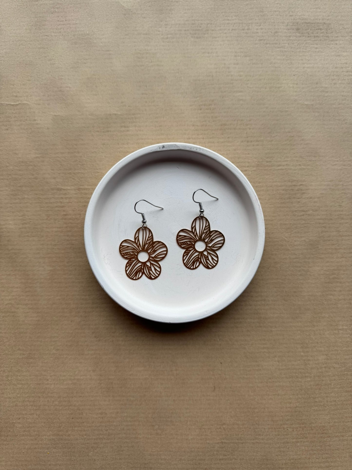 Floral earrings on a white dish with a brown background
