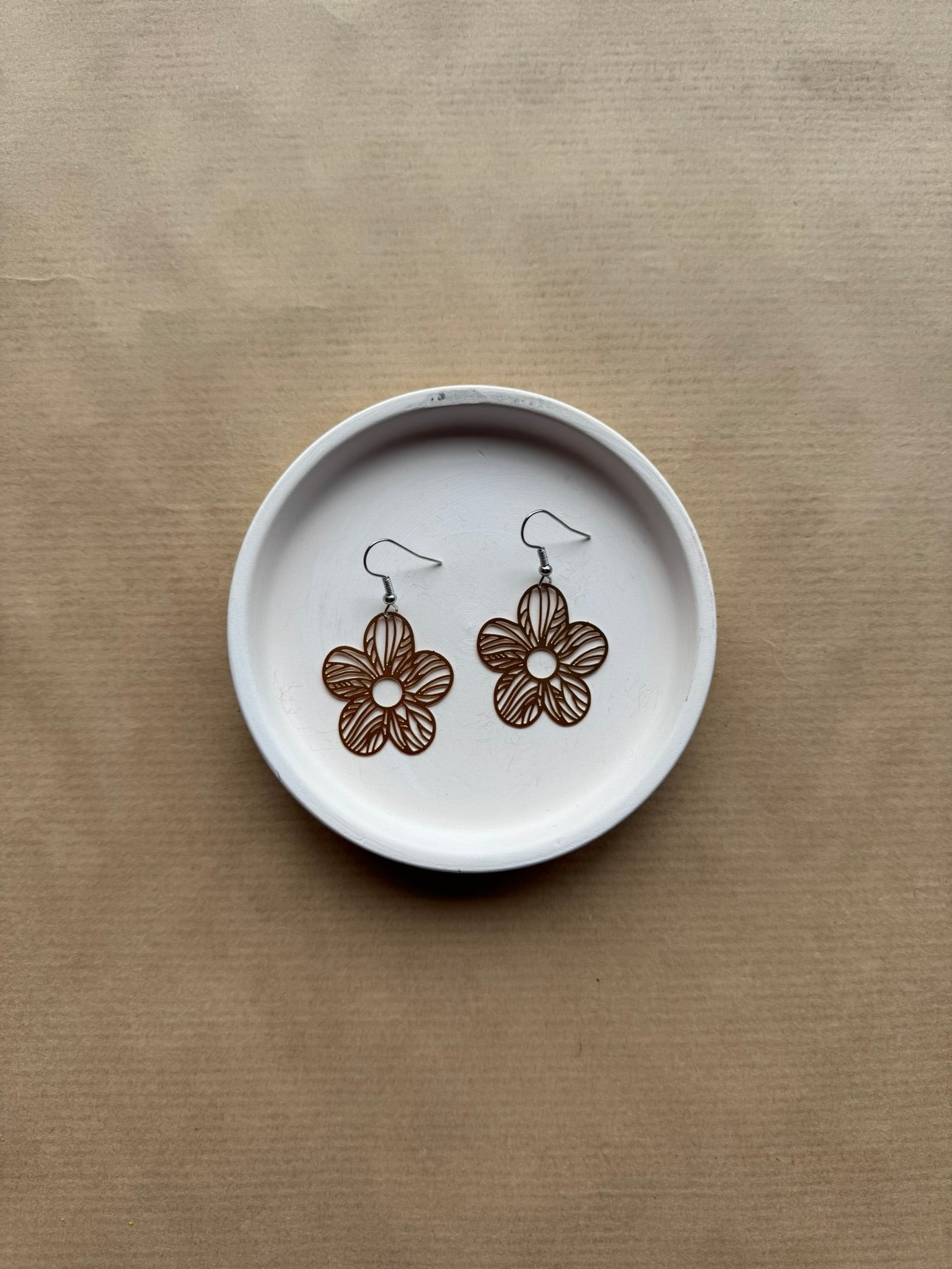 Floral earrings on a white dish with a brown background