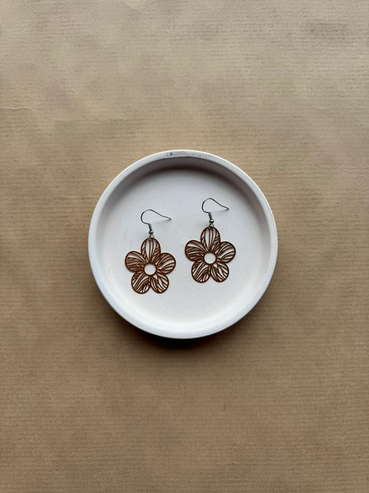 Floral earrings on a white dish with a brown background