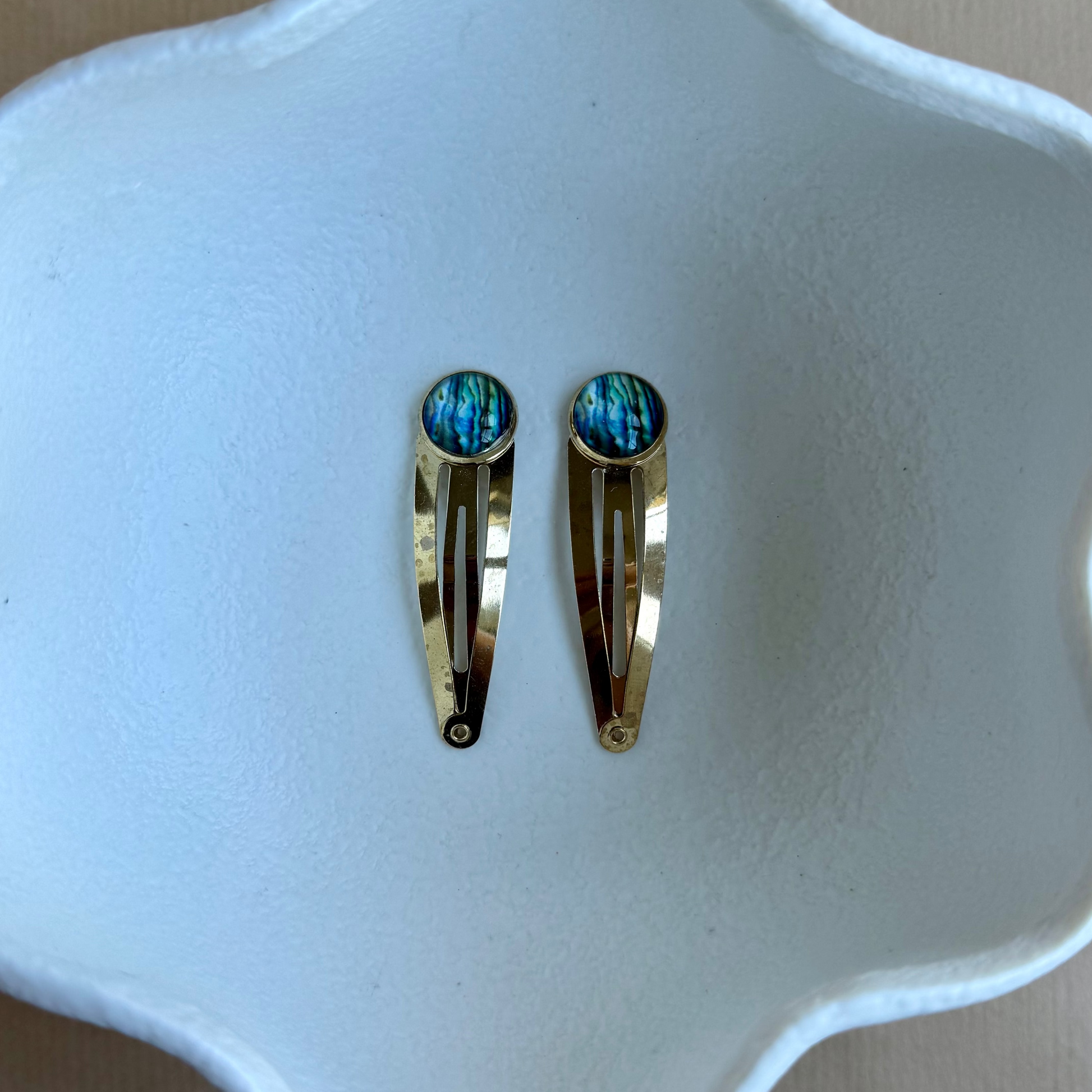 Two gold hair clips with blue stones on a white dish.