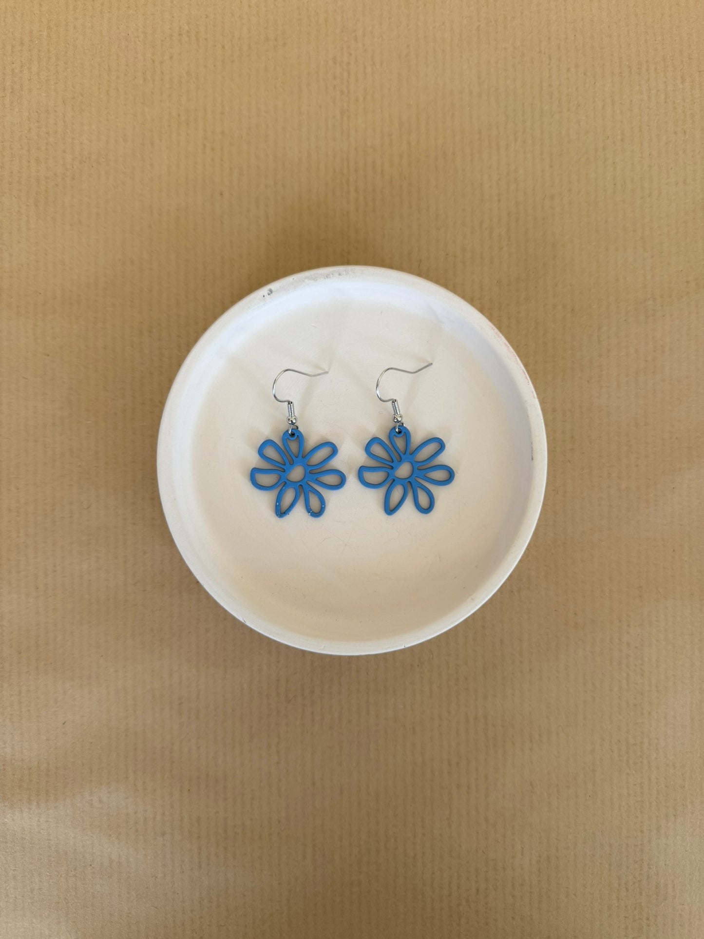 Blue flower-shaped earrings on a white dish against a beige background